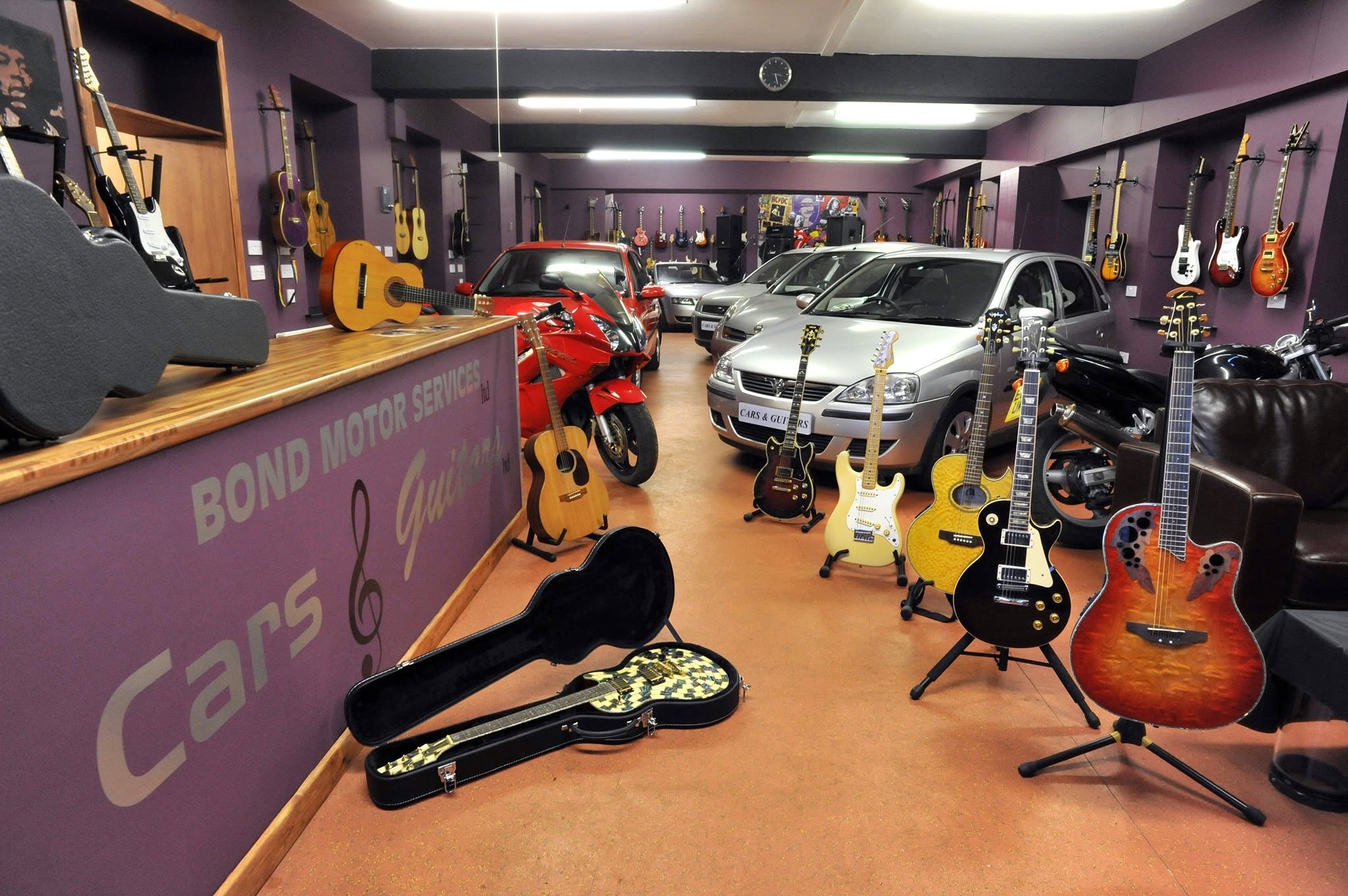 The Bond Motor Services showroom: used cars and a motorbike on the floor, guitars on stands between them and dozens more on the purple walls, and a counter painted Cars & Guitars