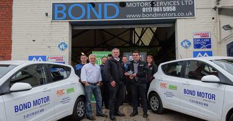 Gary Bond and the team outside the garage with their award, between two Bond Motor courtesy cars